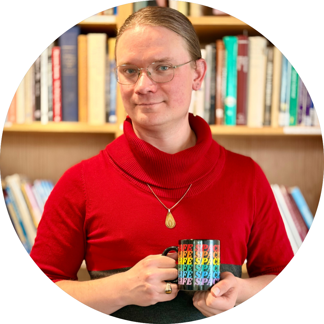 The site author, Birch Cue: white, blonde, transfeminine person in their 30s with wire-rim glasses and hair pulled back. They are wearing a red, black, and gray turtleneck, and an etched metal chalice pendant. They are holding a black coffee mug with the words SAFE SPACE in rainbow colors. They are standing in front of a bookshelf.